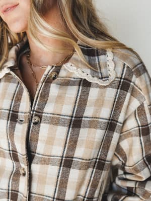 A close-up of a flannel plaid shirt with a unexpected crochet collar detail — the kind of piece that looks like it's been in someone's wardrobe forever but still turns heads at brunch.