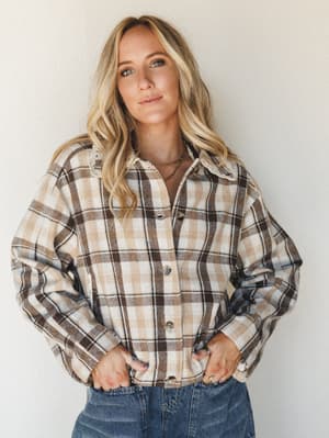 A relaxed plaid flannel shacket in warm cream and mocha tones, styled with denim and layered necklaces — the kind of top that makes a Saturday morning feel intentional.