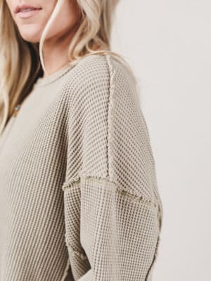 Close-up of a person wearing a beige textured sweater with a blurred background