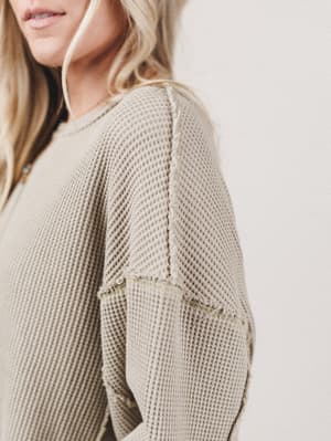 Close-up of a person wearing a beige textured sweater with a blurred background