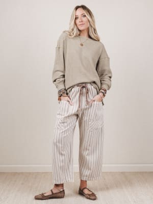 Woman wearing a beige sweater and striped pants against a plain background