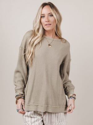 Woman wearing a beige long-sleeve top with pocket details on a plain background