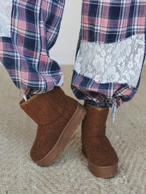 A close-up of tan sherpa platform booties paired with plaid wide-leg pants that have a lace hem detail — cozy, textural, and the kind of outfit you'd actually wear on a slow Saturday morning.