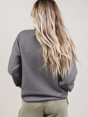 Person wearing a gray sweatshirt with long blonde hair, standing against a plain background