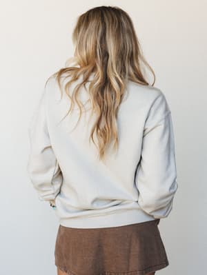 A back-view shot of a relaxed cream crewneck sweatshirt paired with a brown mini skirt — the kind of easy, lived-in combo that feels like a Saturday with nowhere to be.
