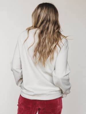 Shot from behind, she's in an oversized sand sweatshirt paired with deep red corduroy pants — the kind of effortless, lived-in combo that looks like it happened on purpose.