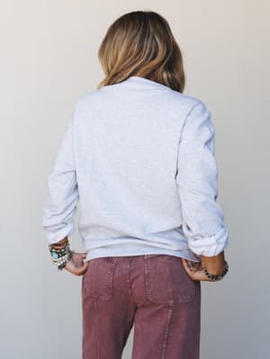 A back-view shot of a model in a heathered ash crewneck sweatshirt paired with dusty mauve wide-leg pants, stacked boho bracelets adding just the right amount of personality to an otherwise effortlessly relaxed look.