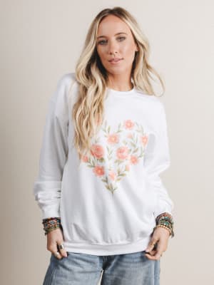 Woman wearing a white sweatshirt with floral design on a beige background