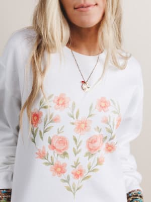 Person wearing a white sweatshirt with floral designs on a plain background
