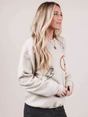 Woman wearing a beige sweatshirt with colorful designs on a plain background