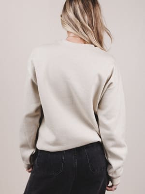 Person wearing a beige sweater and dark pants against a plain background