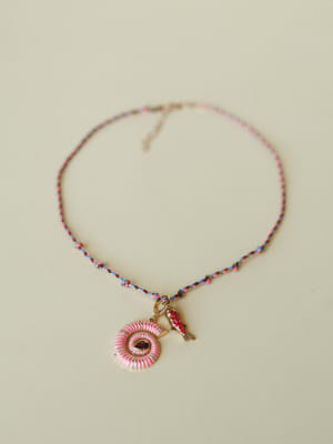 A braided multicolor cord necklace laid flat, featuring a pink enamel spiral shell pendant with a deep red gemstone center and a small gold koi fish charm alongside it — playful and personal, like something you'd pick up on a trip and never take off.