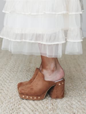A close-up detail shot of caramel suede platform clogs styled with a tiered tulle skirt — the kind of unexpected pairing that makes the whole outfit.