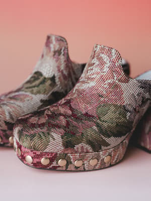 A close-up of tapestry-covered platform clogs with gold stud trim along the sole — the kind of shoes that make an outfit feel intentional without trying too hard.