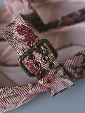 Fabric belt with floral pattern and brass buckle on a neutral background