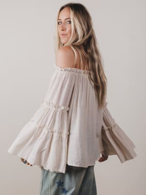 Woman wearing a light-colored off-shoulder top with a plain background