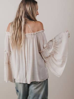 Woman wearing a light-colored off-shoulder blouse with long sleeves against a plain background