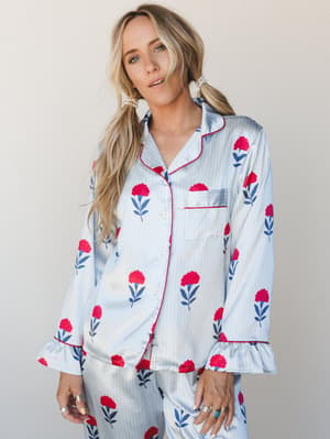 A satin pajama set in soft powder blue with a bold red carnation floral print — the kind of set that makes staying in feel like an occasion.