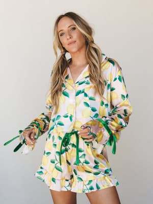 A lemon-print satin matching set — button-up shirt and ruffle-hem shorts — styled with green velvet ribbon ties at the wrists and waist, giving it that effortless 'I woke up like this but make it intentional' energy.