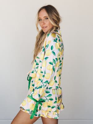 A lemon-print satin pajama short set styled on a model against a neutral studio wall — the kind of set that makes Saturday mornings feel like a Amalfi Coast fantasy.