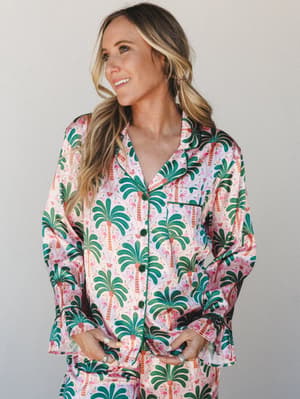 A satin pajama set in a vibrant palm tree and flamingo print — the kind of set that makes staying in feel like a destination.