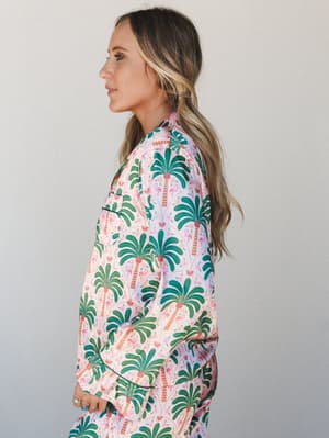 A side-profile shot of a model in a satin-finish pajama set covered in a bold palm tree and flamingo print — the kind of set you'd actually want to be seen in, not just sleep in.