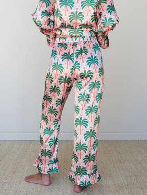 A matching palm tree and flamingo print pajama set shot from the waist down — the kind of set that makes staying in feel just as intentional as going out.