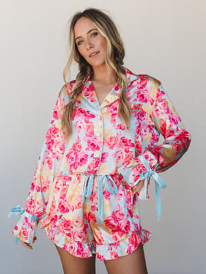 A satin floral pajama set in sky blue and hot pink roses — the kind of set that makes staying in feel like a whole occasion.