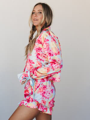 A floral satin PJ short set in sky blue and hot pink roses, styled with a side braid and pearl hair accessory — equal parts cozy morning energy and the kind of thing you'd wear to a bachelorette that gets photographed.