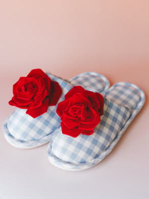 Gingham slide slippers in soft powder blue get a romantic upgrade with bold red velvet rosette embellishments — cozy-meets-whimsical, shot against a blush backdrop.
