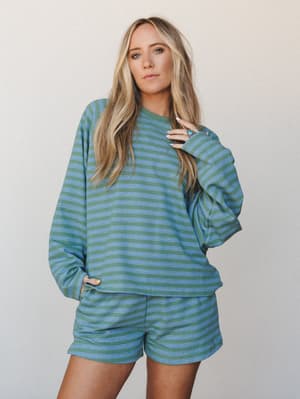 A matching striped sweatshirt-and-shorts set in sage green and periwinkle blue, styled casually on a model against a neutral studio backdrop — the kind of set that makes staying in feel like a whole personality.