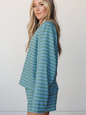 A relaxed striped short set in sage green and periwinkle blue, shot in profile against a soft neutral wall — the kind of matching set that makes staying home feel intentional.