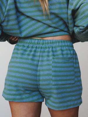 A close-up back view of a matching striped short set in sage green and cobalt blue — the relaxed pull-on shorts and long-sleeve top feel like the kind of set you wear on a slow Saturday and somehow never want to take off.