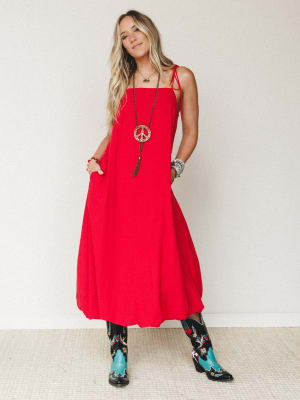 A bold red maxi bubble dress with tie straps and side pockets, styled with embroidered western cowboy boots and a long peace sign pendant necklace — free-spirited and full of personality.
