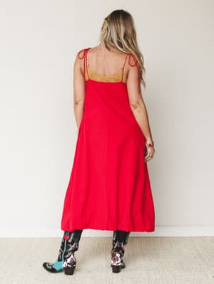 A bold red maxi dress with tie shoulder straps and a gold embroidered bodice, styled back-to-camera with statement embroidered cowboy boots — the kind of outfit that walks into a room before you do.