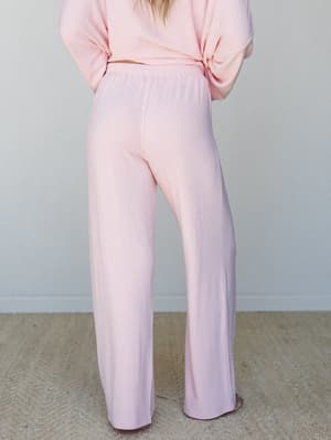 Shot from behind, a model wears a soft blush pink wide-leg pant with a matching oversized top — the kind of set that makes staying home feel intentional.