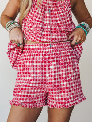 A matching red and pink gingham set with tiny heart print — the shorts take center stage with their ruffle hem and elastic waist, styled with stacks of turquoise and beaded bracelets for that effortless boho-meets-playful energy.