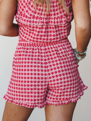 A close-up back view of red gingham shorts with a sweet heart print and ruffle hem, styled with stacked turquoise and gold bracelets — playful and a little nostalgic in the best way.