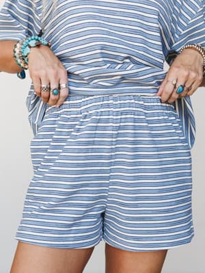 A close-up mid-shot of a matching striped set — cropped top and pull-on shorts in soft blue and cream — styled with layers of turquoise and silver boho jewelry for that effortless, collected summer feel.