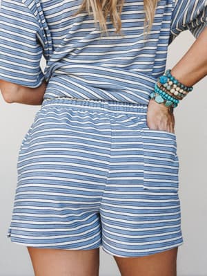 A close-up back view of a matching blue and white stripe shorts set, styled with a stack of turquoise and mixed bead bracelets — casual and collected with just enough personality in the accessories.