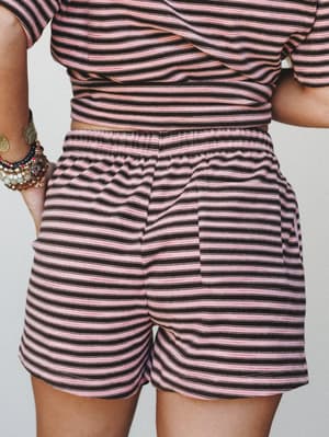 A close-up back view of relaxed striped shorts in pink and dark brown, paired with a matching striped top and stacked bracelets — the kind of effortless set that feels like a lazy Saturday and a good mood at the same time.