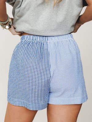 A mixed-print shorts moment that earns a second look — gingham on one side, seersucker stripes on the other, styled casually with a gray tee and stacked turquoise bracelets.