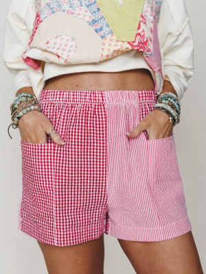 A playful mix-and-match moment — color-blocked shorts pair red gingham and pink stripe panels side by side, worn with a patchwork sweatshirt and stacked beaded bracelets that feel like they've been collected over a lifetime.
