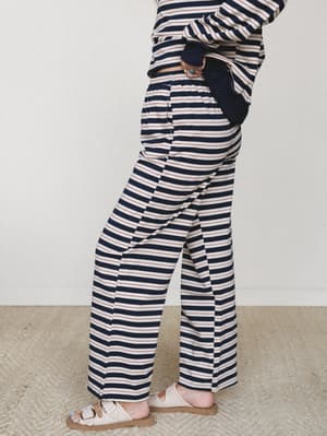 A relaxed wide-leg striped pant in a classic navy and cream Breton stripe with a thin red accent line, styled as a matching set with a long-sleeve top and worn with white buckle sandals — easy, lived-in, and a little nautical.