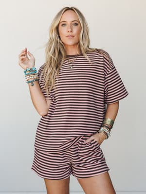 A matching striped tee-and-shorts set in dusty pink and charcoal, styled with stacks of boho bead bracelets and a layered gold necklace — casual and collected, like a weekend that actually went well.