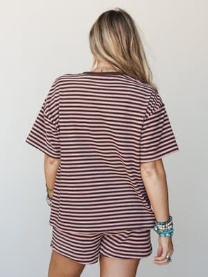 A matching striped tee-and-shorts set shot from the back, styled with stacked turquoise and beaded bracelets — relaxed and effortlessly put-together in a pink and dark brown stripe.