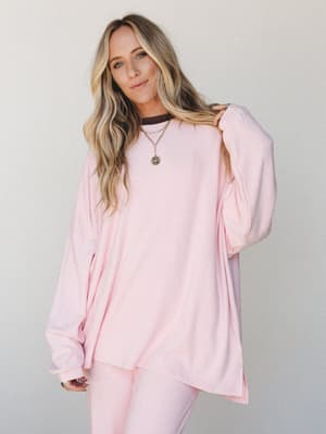 An oversized soft pink long-sleeve top styled as a matching set, worn with layered gold necklaces against a clean light backdrop — the kind of effortless cozy-cool that makes you want to cancel plans and stay in it all day.