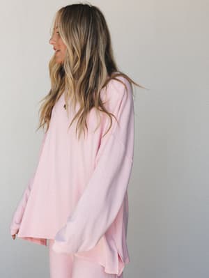 A relaxed, oversized long sleeve top in the softest blush pink, styled as a matching set and shot from a side angle — the kind of effortless outfit that makes staying in feel intentional.