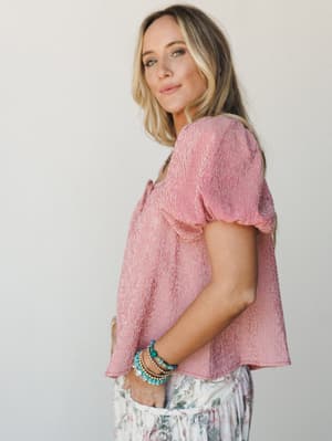 A breezy red gingham puff-sleeve top styled with a floral skirt and stacked turquoise bracelets — the kind of outfit that feels equally at home at a farmers market or a backyard birthday party.