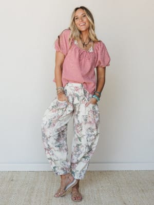 A smiling model in a red gingham peasant top and cream floral jogger pants — the kind of mix-and-match energy that looks effortless but is clearly very much on purpose.